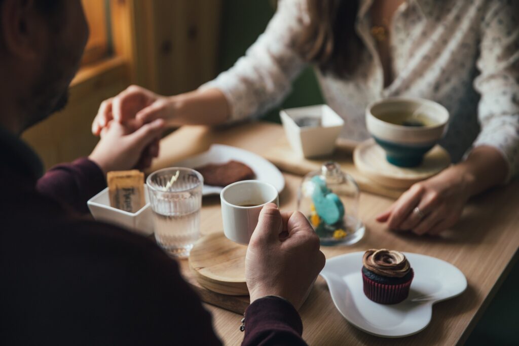 Two people sitting in a restaurant. The image shows a close-up of the couple's hands as they have coffee and pastry.