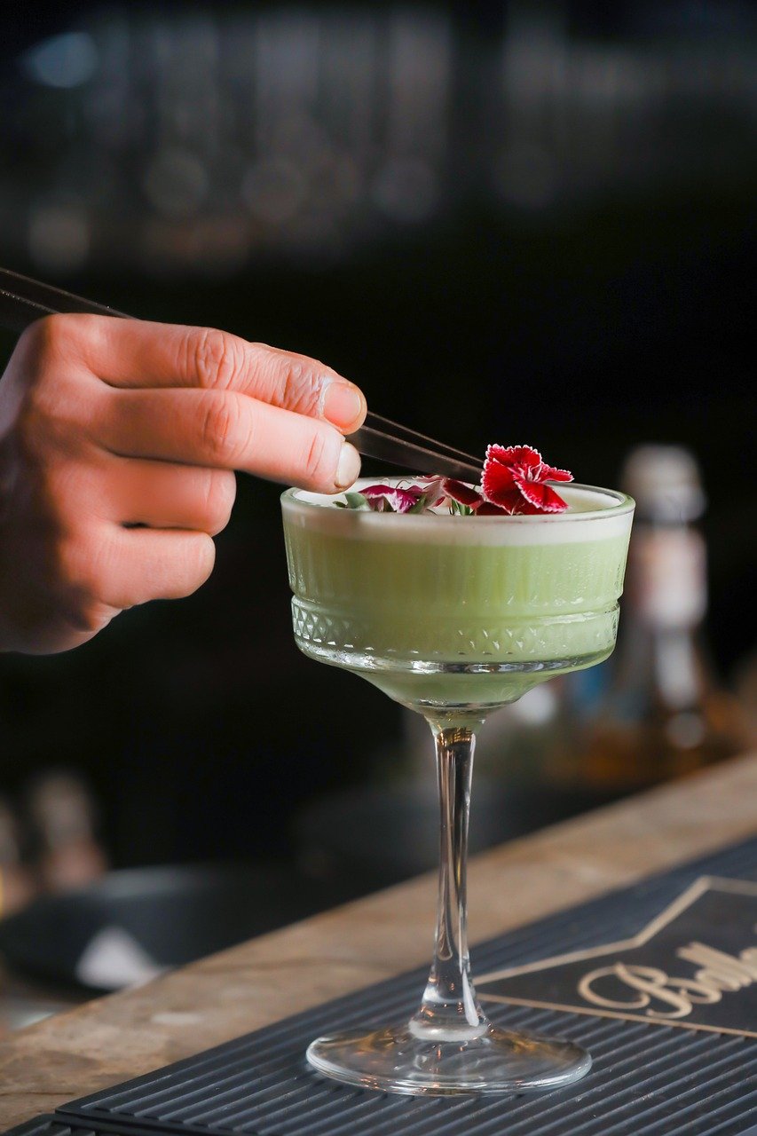 Flowers being placed artfully on a green-colored cocktail as part of experience design.